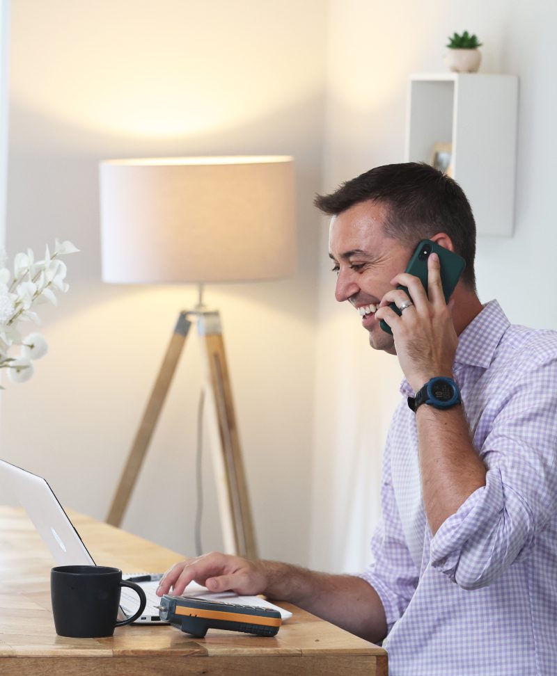 A man sitting at a desk, talking on the phone with a happy expression.