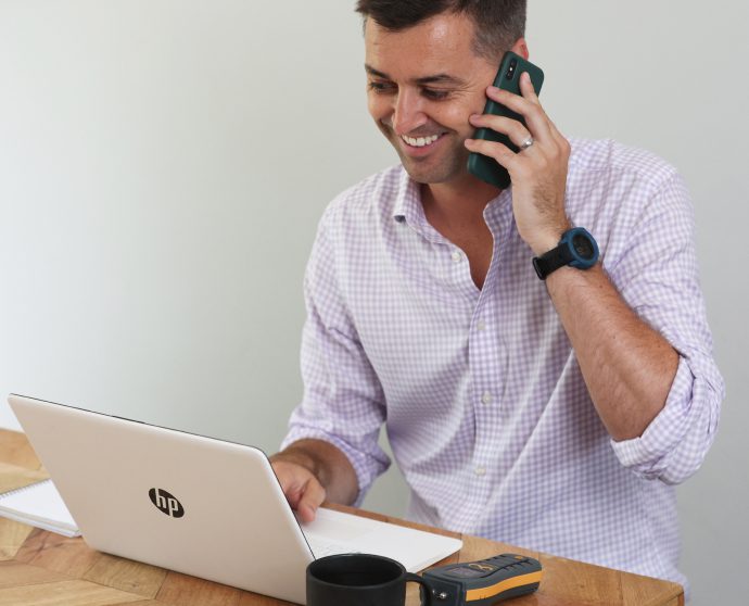 A man working at a desk with a laptop and a cell phone in front of him.